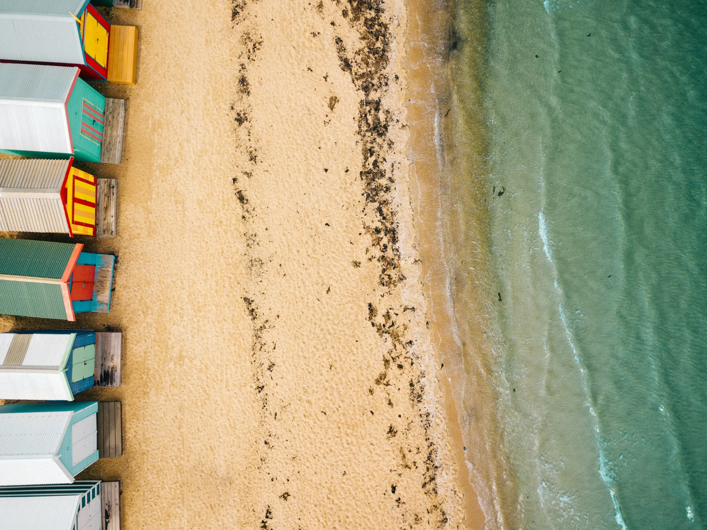 Aerial view of Brighton's colourful bathing boxes on a sunny Melbourne beach